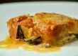 Primo piano di una fetta di parmigiana di melanzane con strati di salsa di pomodoro, formaggio fuso e melanzane al forno su un piatto bianco, presentata da Giorgio di Cucino di Te, chef a domicilio a Varese.
