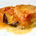 Primo piano di una fetta di parmigiana di melanzane con strati di salsa di pomodoro, formaggio fuso e melanzane al forno su un piatto bianco, presentata da Giorgio di Cucino di Te, chef a domicilio a Varese.